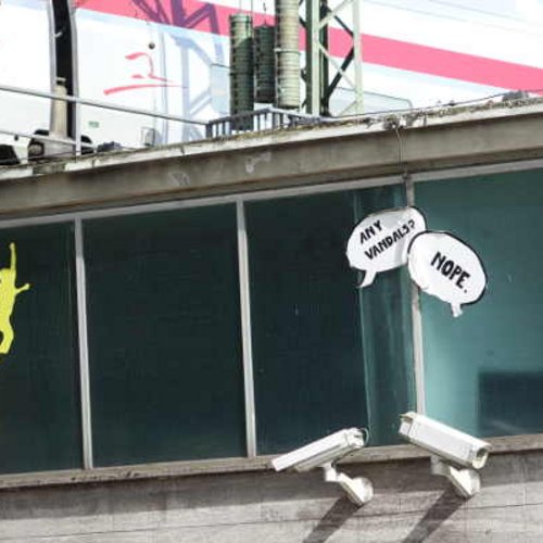 Zwei Videokameras an einer Hauswand. Auf die Hauswand geklebte Sprechblasen: "Any vandals?" / "Nope."